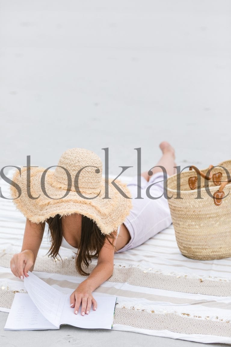 Vertical stock photo of woman reading magazine at the beach