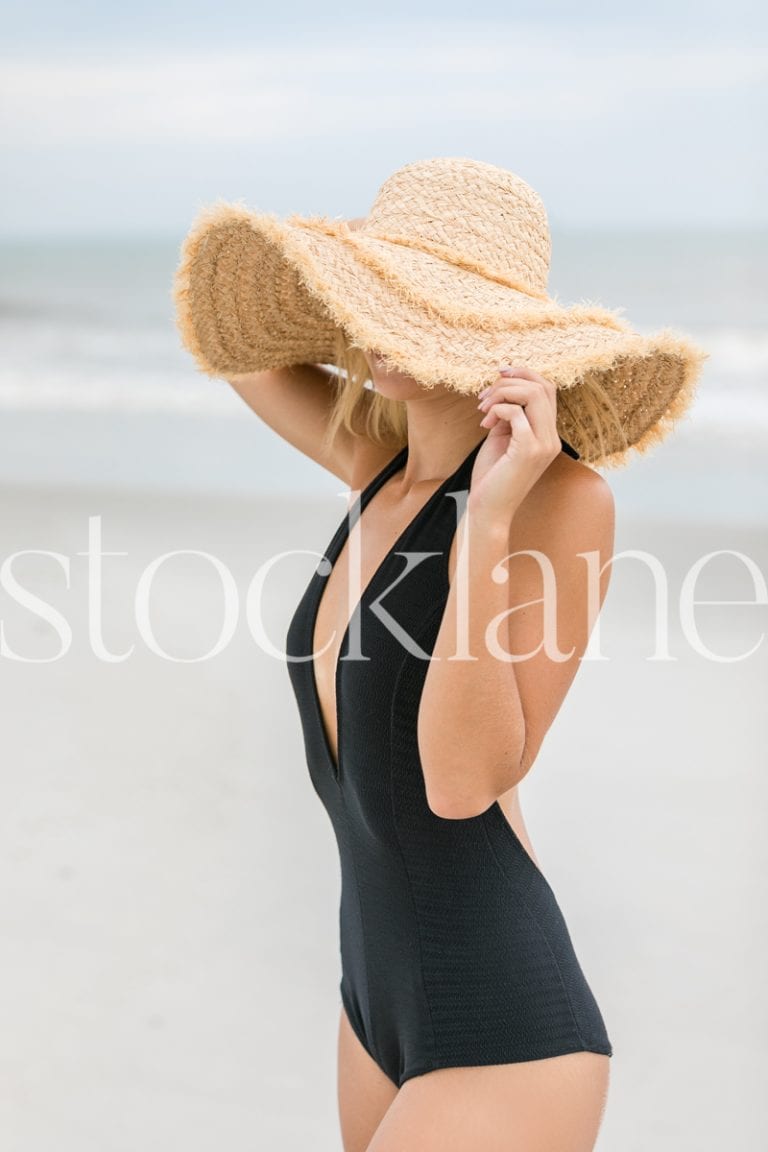 Vertical stock photo of woman with big hat at the beach