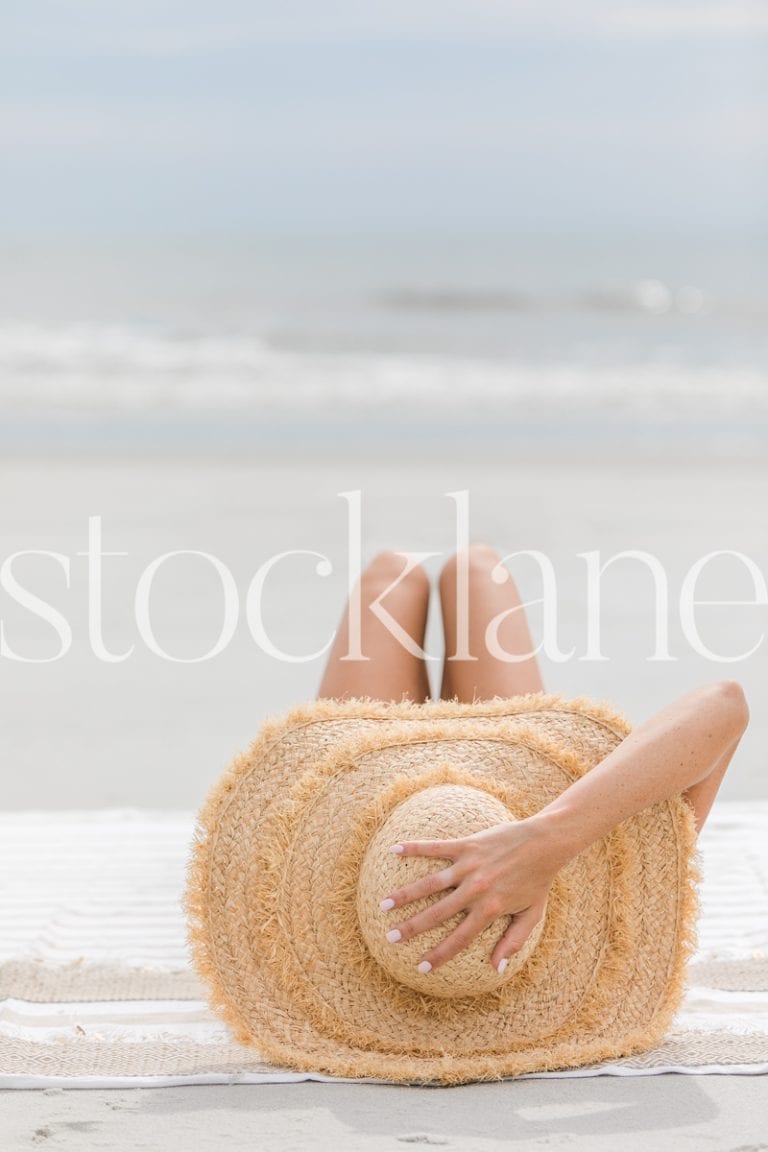 Vertical stock photo of woman with large hat at the beach