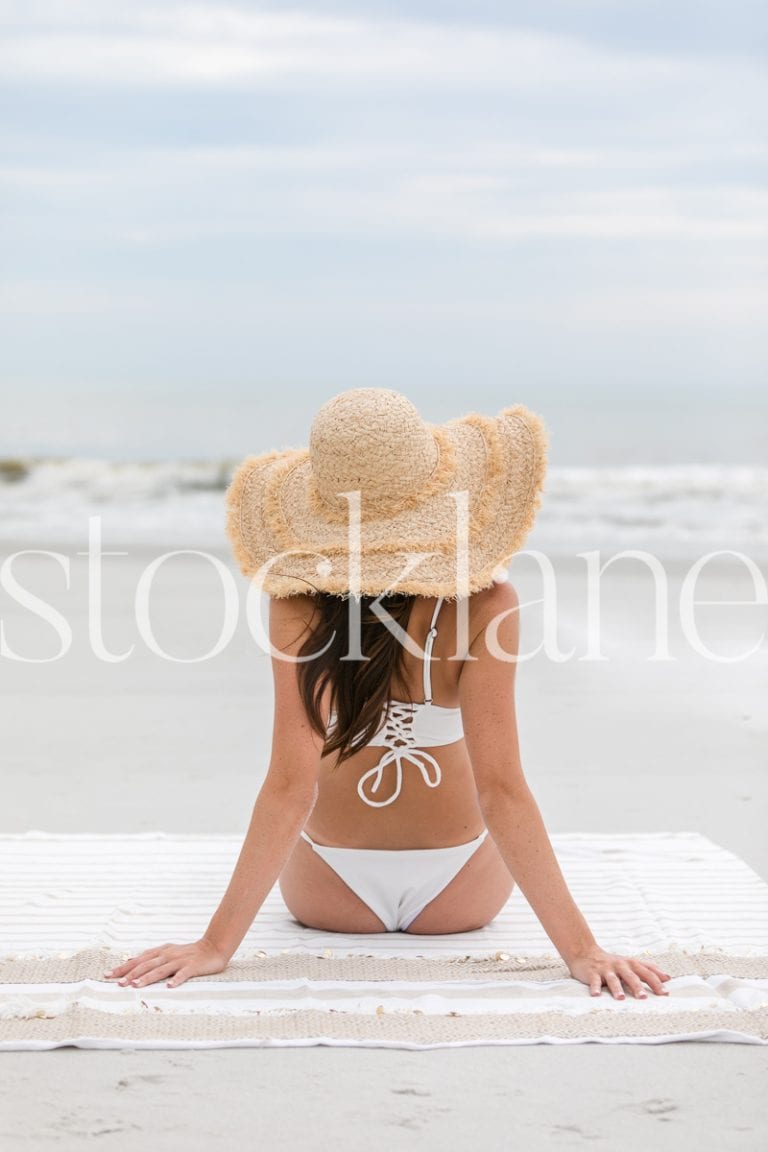 Vertical stock photo of woman with large hat at the beach