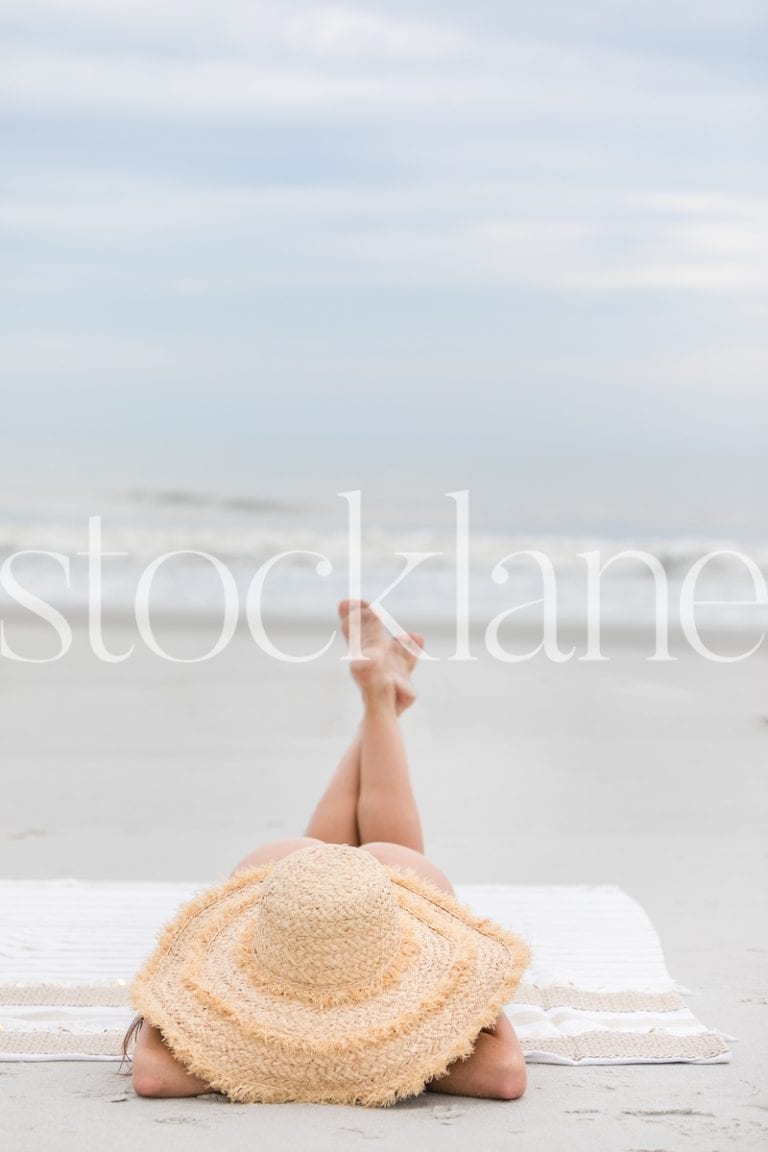 Vertical stock photo of woman with large hat at the beach