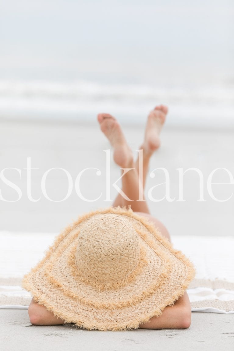 Vertical stock photo of woman with large hat at the beach