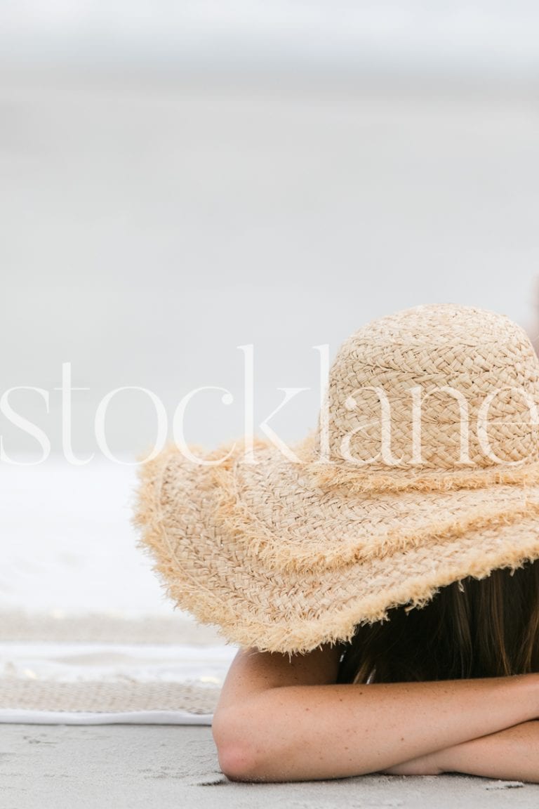 Vertical stock photo of woman with large hat at the beach