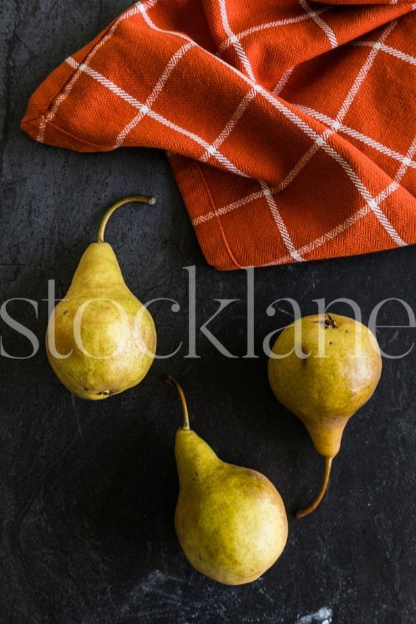 Vertical stock photo of pears in dark background with orange kitchen cloth