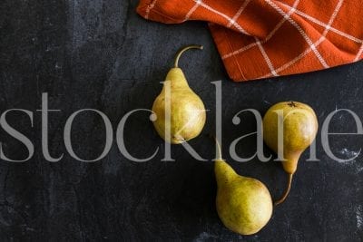 Horizontal stock photo of pears in dark background with orange kitchen cloth