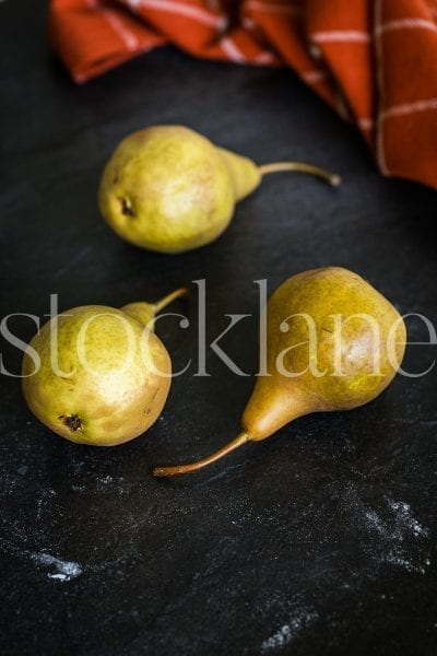 Vertical stock photo of pears in dark background with orange kitchen cloth