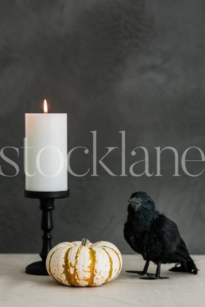 Vertical Halloween stock photo of white candle, white pumpkin and crow