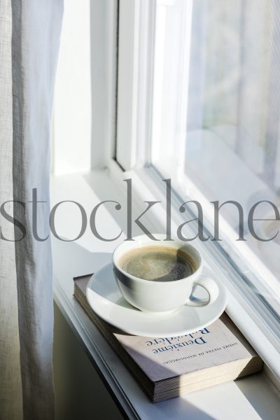 Vertical stock photo of coffee cup and book on window