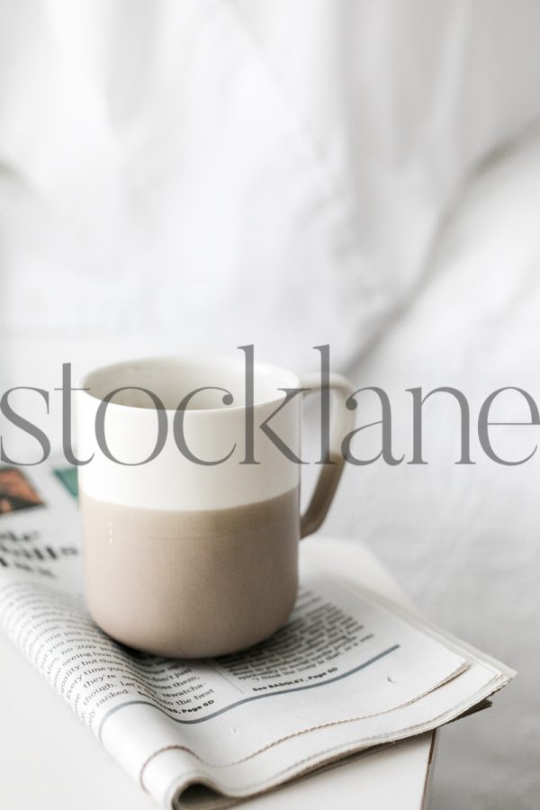 Vertical stock photo of coffee mug and newspaper on nightstand