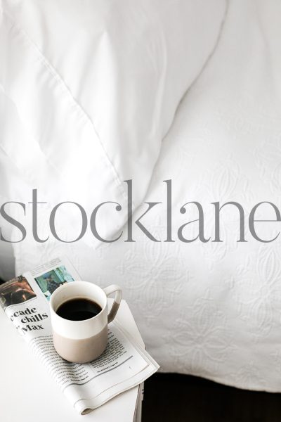 Vertical stock photo of coffee mug and newspaper next to bed