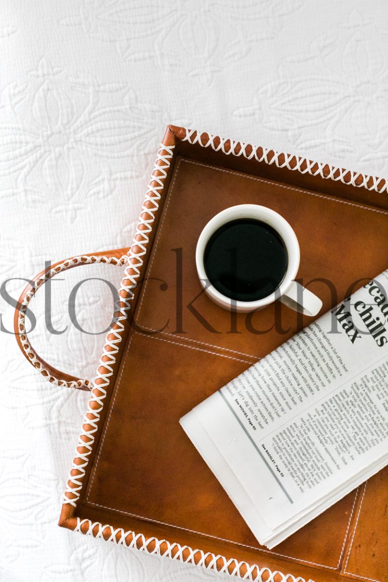 Vertical stock photo of a tray on a bed with coffee and newspaper