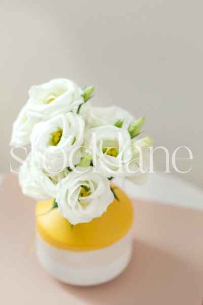 Vertical stock photo of bright yellow flower vase on pink notebooks