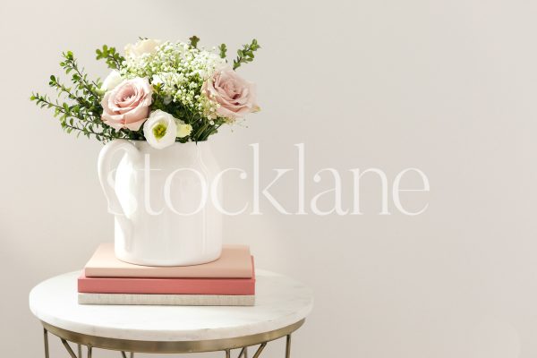 Horizontal stock photo of white vase with white and pink flowers on top of pink notebooks