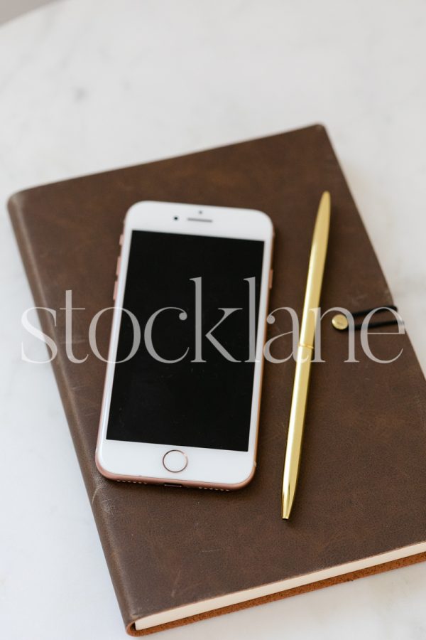 Vertical stock photo of brown notebook with gold pen and phone