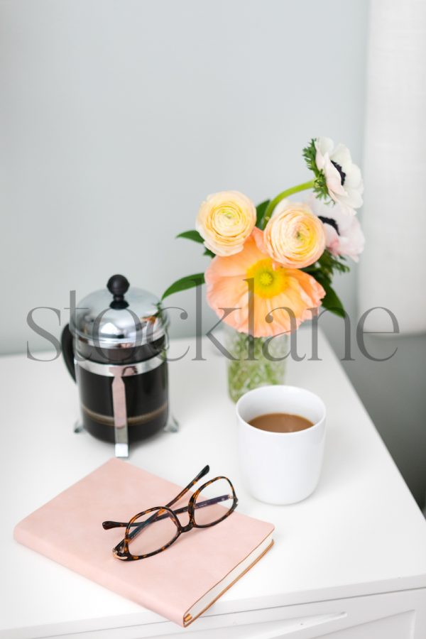 Vertical stock photo of feminine nightstand with coffee, flowers and notebook