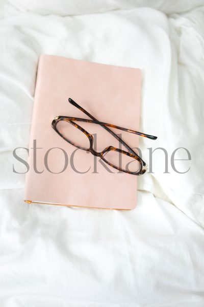 Vertical stock photo of pink book and glasses on a bed