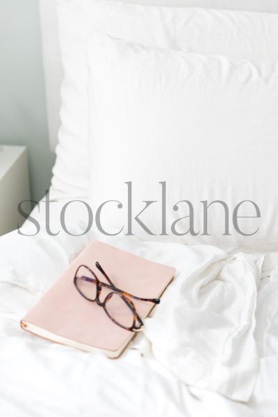 Vertical stock photo of pink book and glasses on a bed