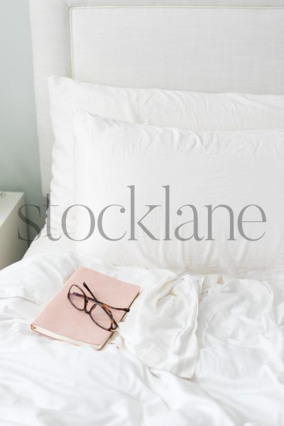 Vertical stock photo of pink book and glasses on a bed