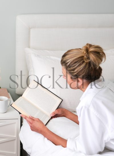 Vertical stock photo of woman reading in bed