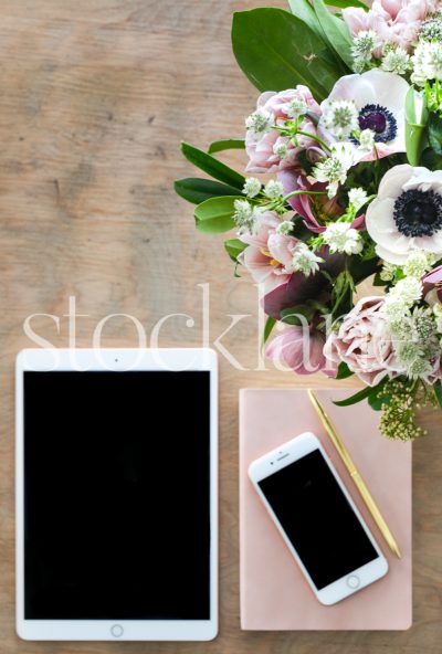 Vertical stock photo of phone and tablet on desk with flowers