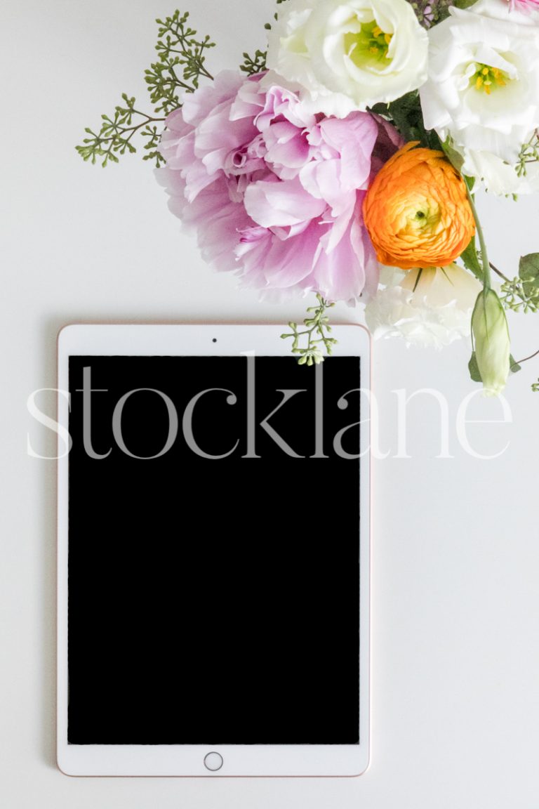 Vertical stock photo of a white tablet with spring flowers.