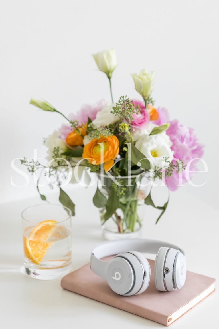 Vertical lifestyle stock photo of a feminine desktop with a pink notebook and white headphones.