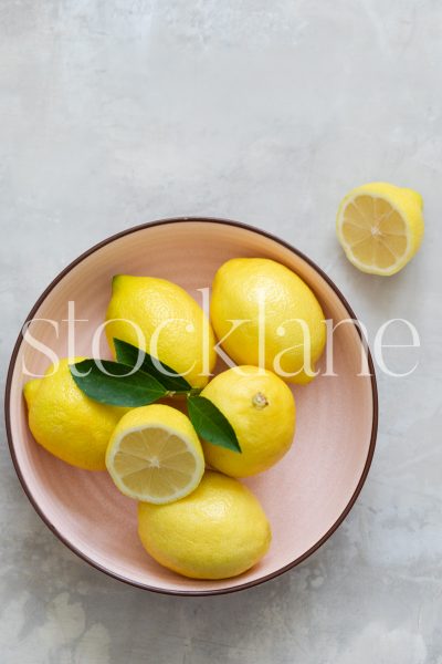 Vertical stock photo of lemons in a pink bowl.