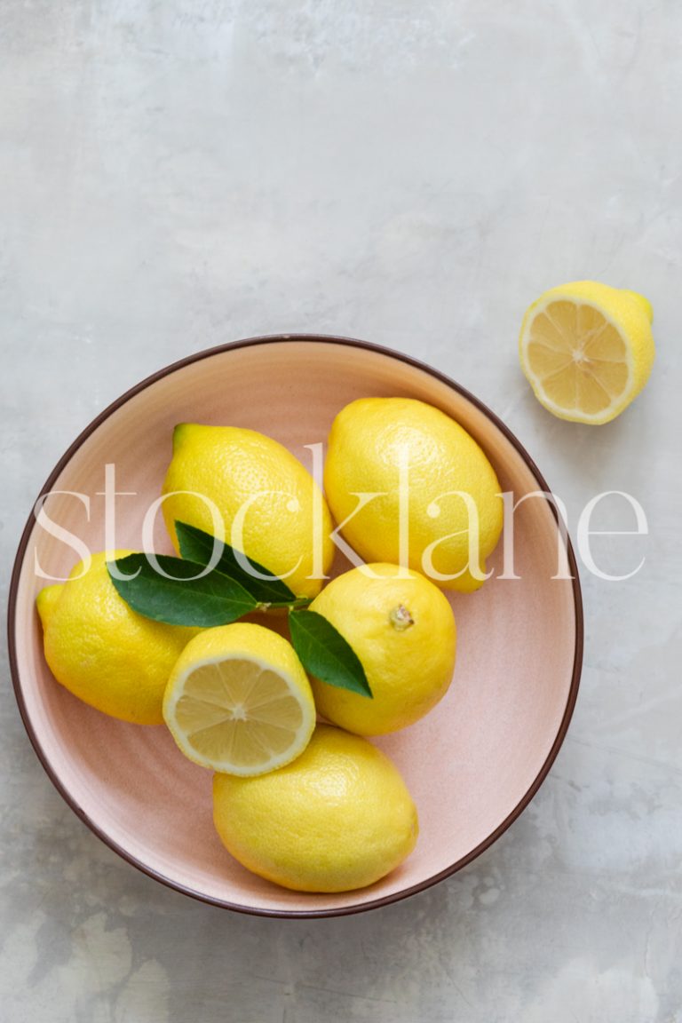 Vertical stock photo of lemons in a pink bowl.