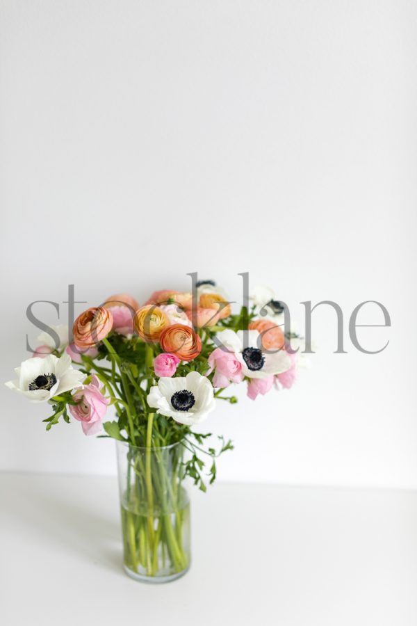 Vertical stock photo of spring flower arrangement with pink ranunculus and white anemone.