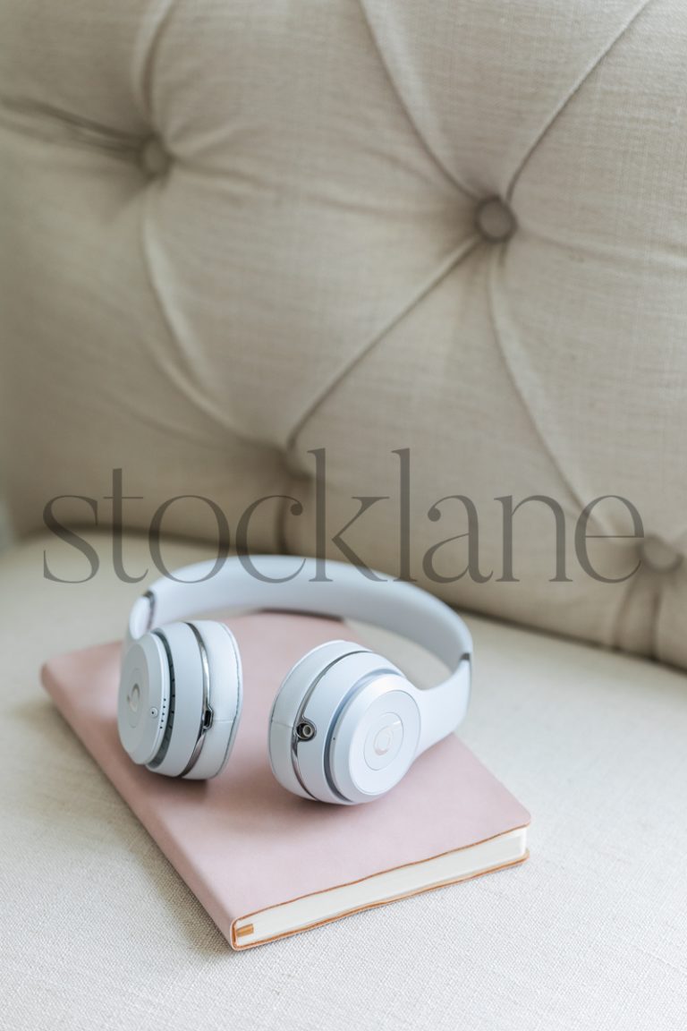 Vertical stock photo of a pink notebook and white headphones on a chair.