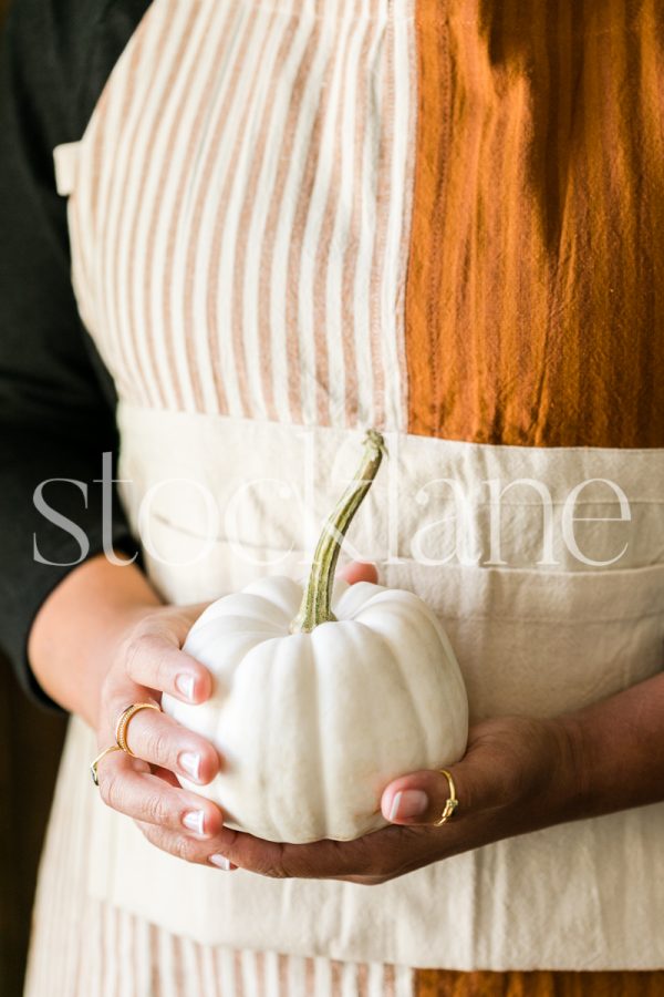 Vertical stock photo of a woman holding a white pumpkin.