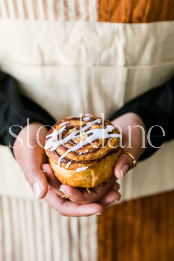 Vertical stock photo of a woman holding a cinnamon roll.