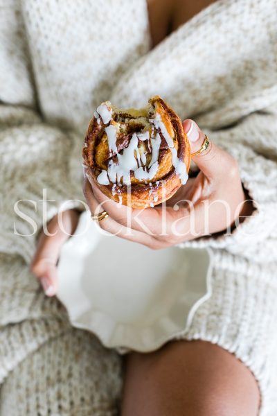 Vertical stock photo of woman eating a cinnamon roll.