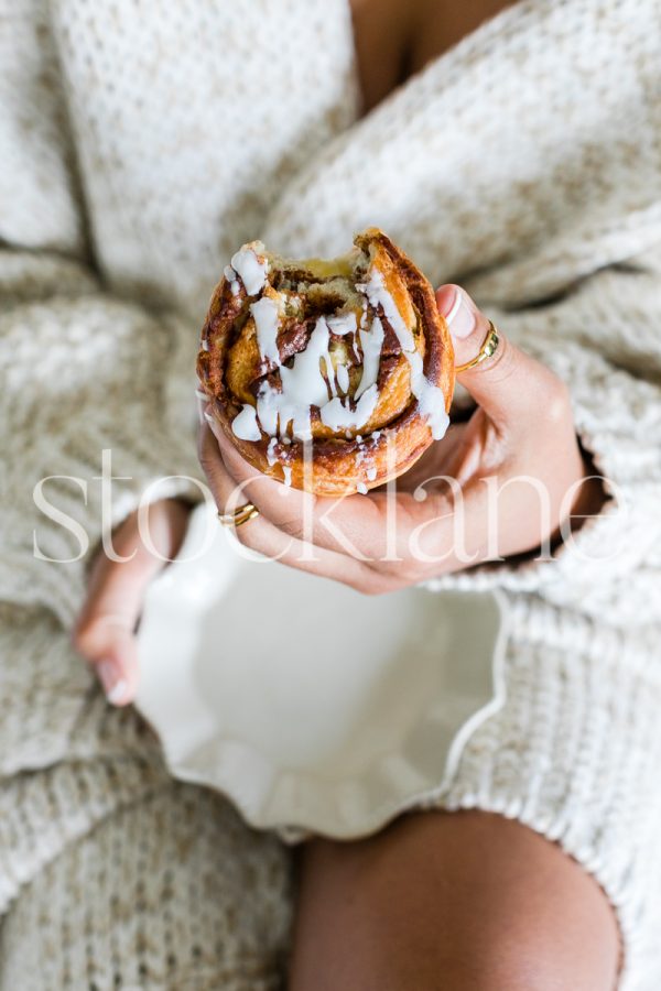 Vertical stock photo of woman eating a cinnamon roll.