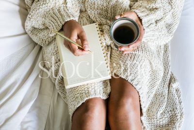 Horizontal stock photo of woman working in bed with coffee and cinnamon roll.