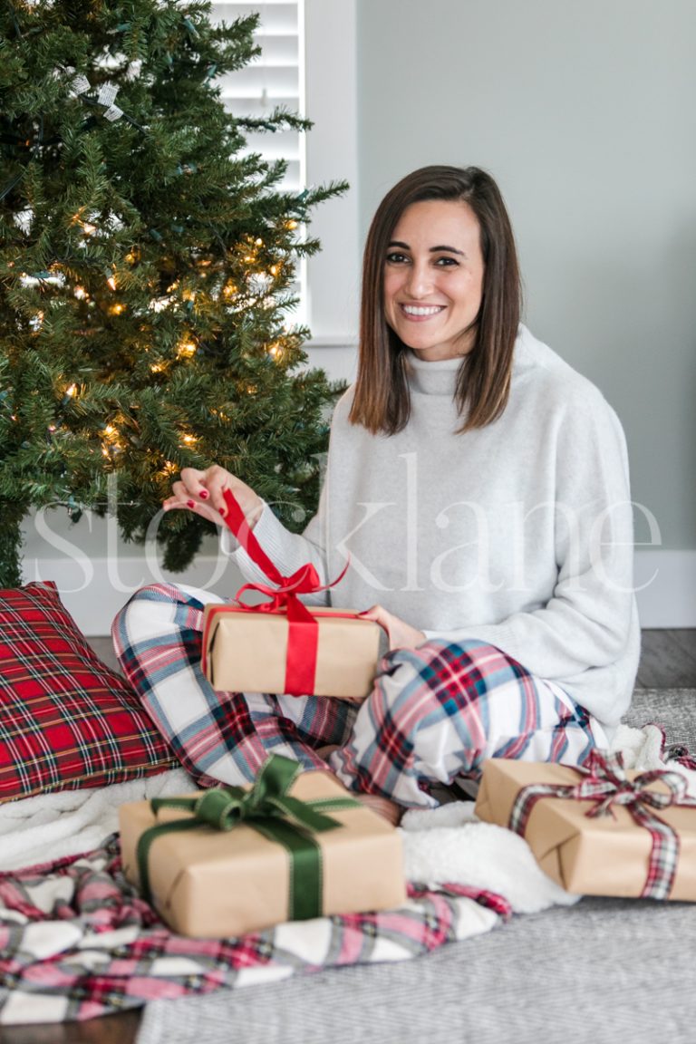 Vertical stock photo of a woman opening a gift on Christmas morning.