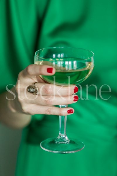 Vertical stock photo of a woman wearing a green dress holding a glass of champagne.