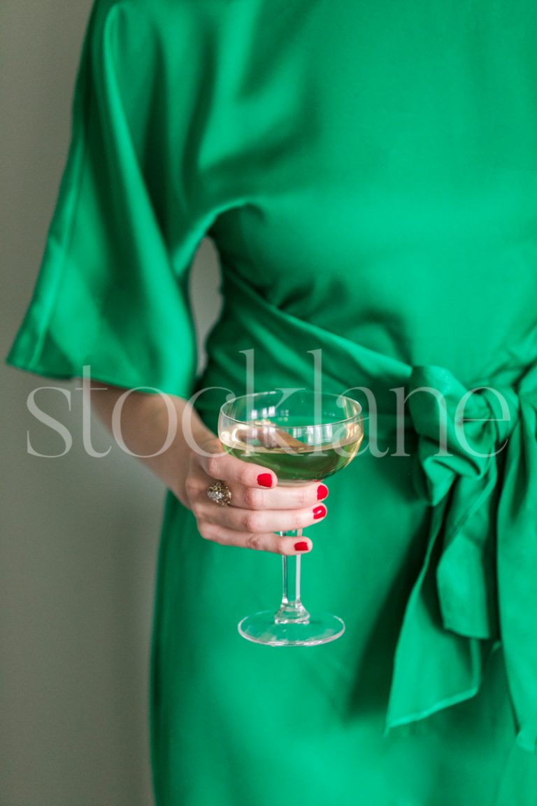 Vertical stock photo of a woman wearing a green dress holding a glass of champagne.