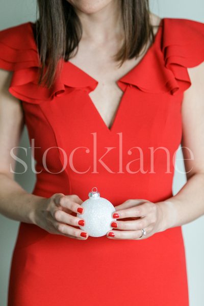 Vertical stock photo of a woman in a red dress holding a Christmas ornament.