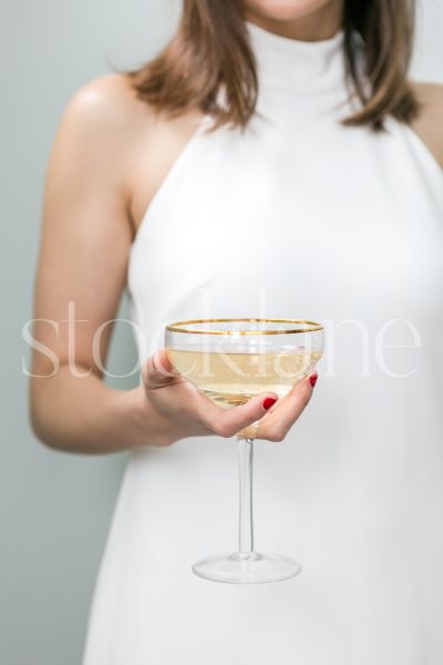 Vertical stock photo of a woman in a white dress holding a glass of champagne.