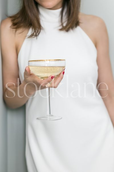 Vertical stock photo of a woman in a white dress holding a glass of champagne.