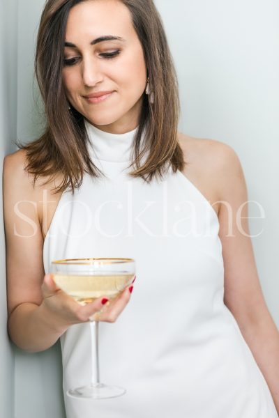 Vertical stock photo of a women in a white dress holding a glass of champagne