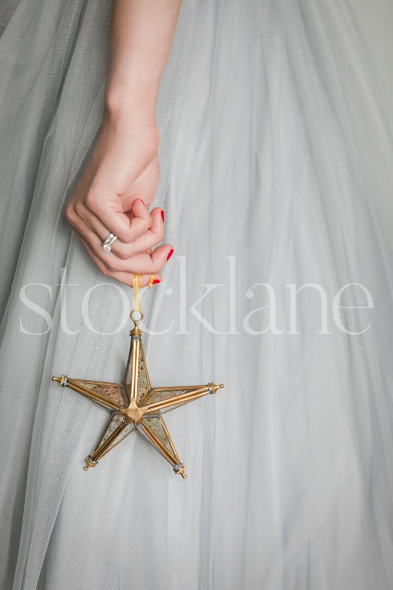 Vertical stock photo of a woman in a light blue dress with a Christmas ornament