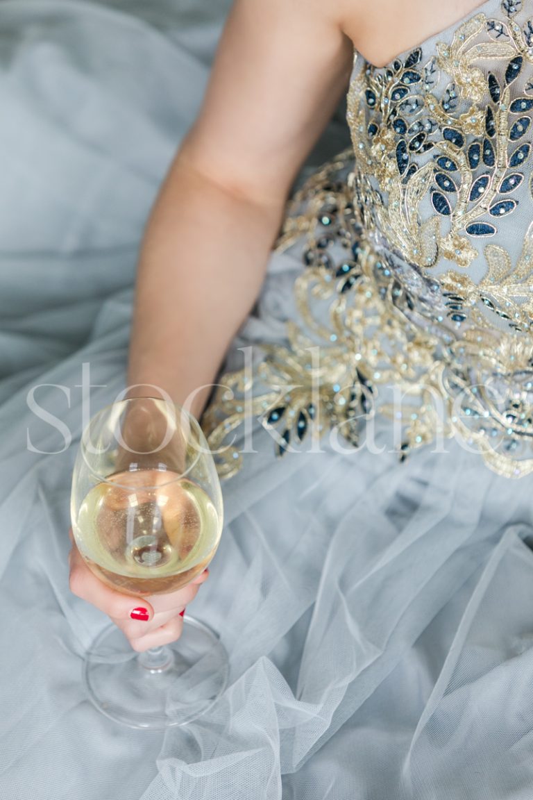 Vertical stock photo of a woman in a light blue dress with a glass of wine