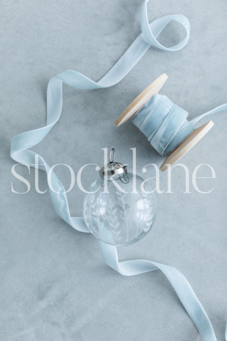 Vertical stock photo of glass Christmas ornament and light blue ribbon.