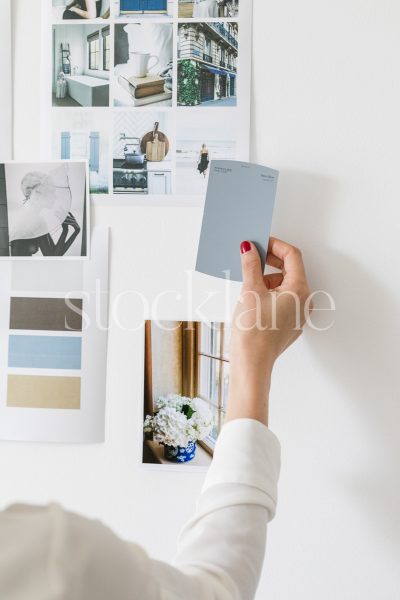 Vertical stock photo of a woman holding a color swatch to a mood board.