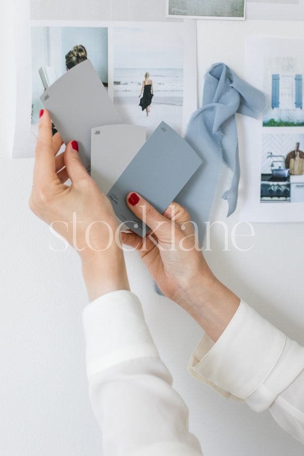 Vertical stock photo of a woman holding a color swatch to a mood board.