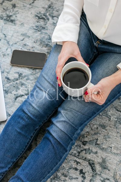 Vertical stock photo of a woman sitting on the floor drinking coffee.