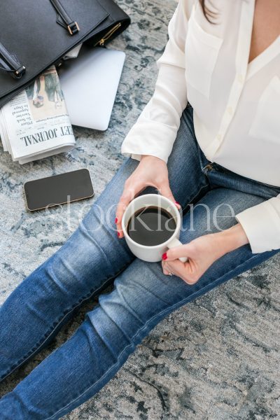 Vertical stock photo of a woman sitting on the floor drinking coffee.