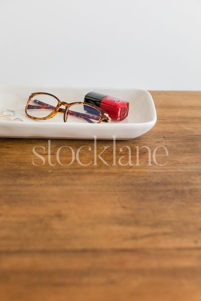 Vertical stock photo of a desk with glasses and red nail polish.